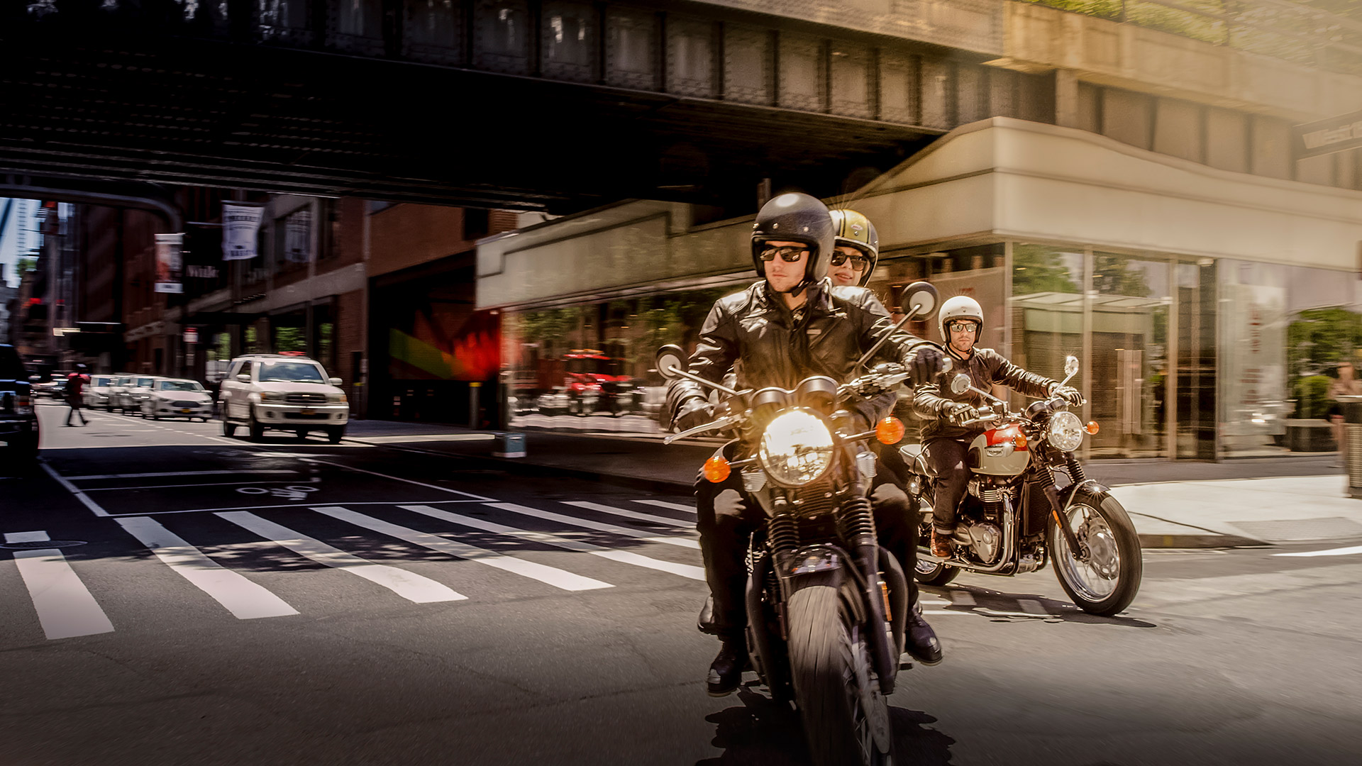 Two Triumph Bonneville T100s riding through a built up urban area.