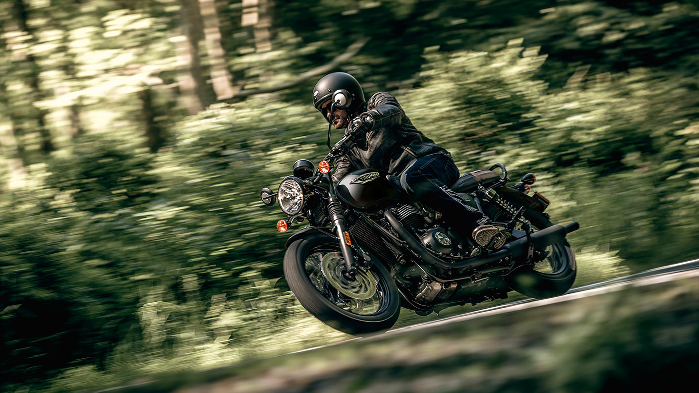 Triumph Bonnevile T120 motorcycle riding around corner in woodlands