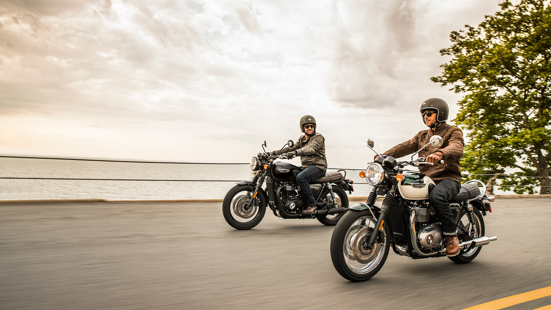 Two men riding Triumph Bonneville T120s down road